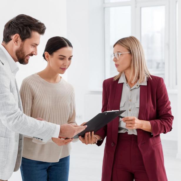 Drei Personen stehen zusammen und betrachten gemeinsam ein Klemmbrett in einem hellen Raum.