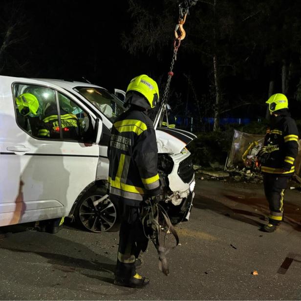 Drei Feuerwehrleute arbeiten nachts an einem stark beschädigten weißen Transporter nach einem Unfall.