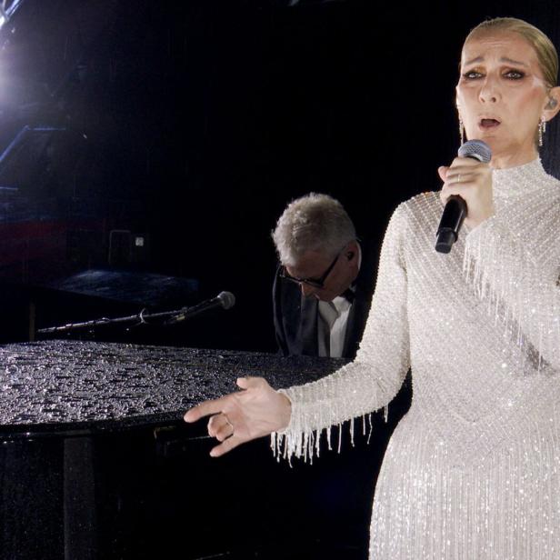 Céline Dion singt in einem glitzernden Kleid neben einem Pianisten vor einem Klavier.