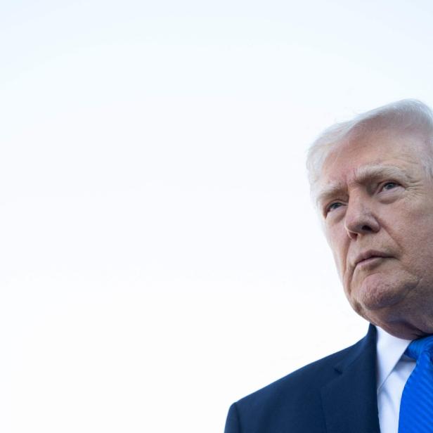 Ein älterer Mann im Anzug mit blauer Krawatte blickt ernst nach vorne, der Hintergrund ist hell und einfarbig.