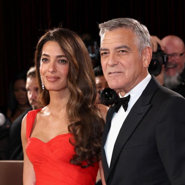 Amal Clooney und George Clooney posieren auf einem roten Teppich.