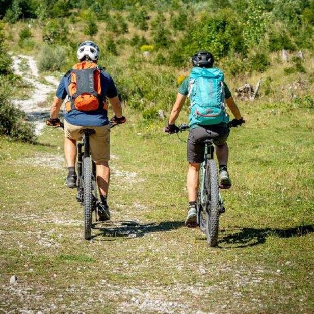 Zwei Radfahrer fahren auf einem Weg vor einer Bergkulisse.