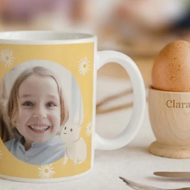 Personalisierte Tasse mit Kinderfoto und Eierbecher mit dem Namen Clara auf einem Frühstückstisch.