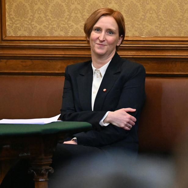 Elke Hanel-Torsch mit kurzem, rötlichem Haar sitzt in einem eleganten Raum auf einer Bank und trägt einen dunklen Blazer.