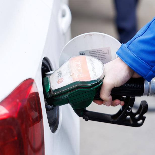 Eine Person tankt ein weißes Auto mit einer grünen Zapfpistole an einer Tankstelle.