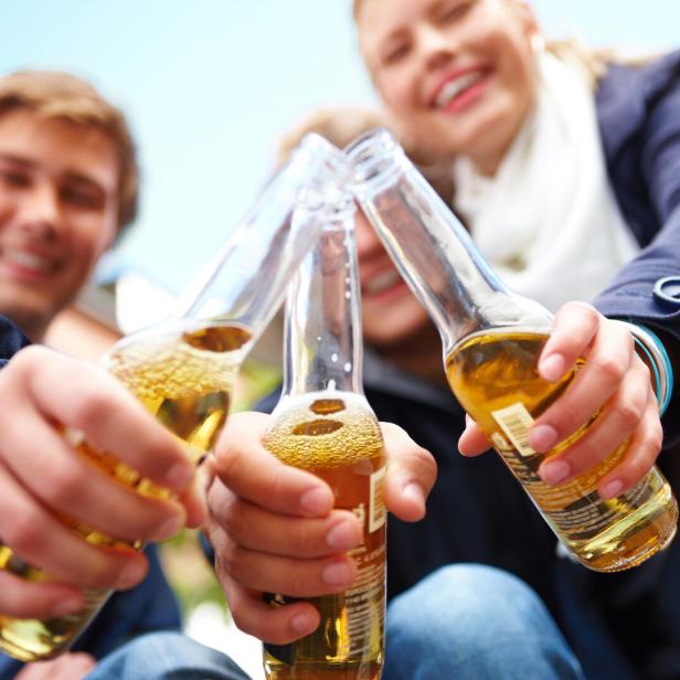 Jugendliche stoßen mit drei Flaschen miteinander an.
