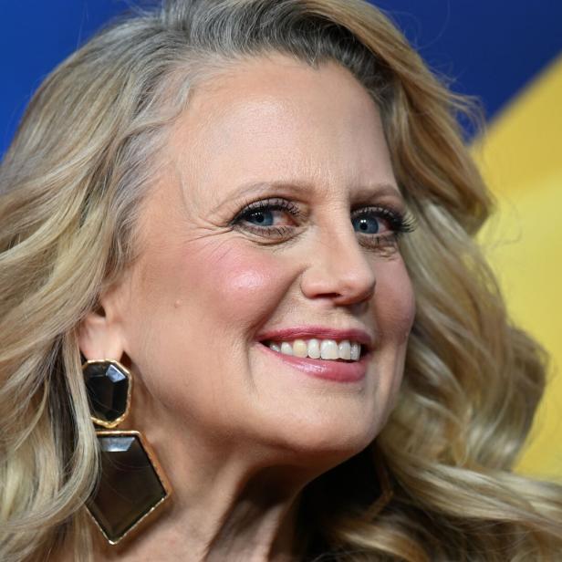 Barbara Schöneberger mit blonden, gewellten Haaren und auffälligen Ohrringen vor farbigem Hintergrund.