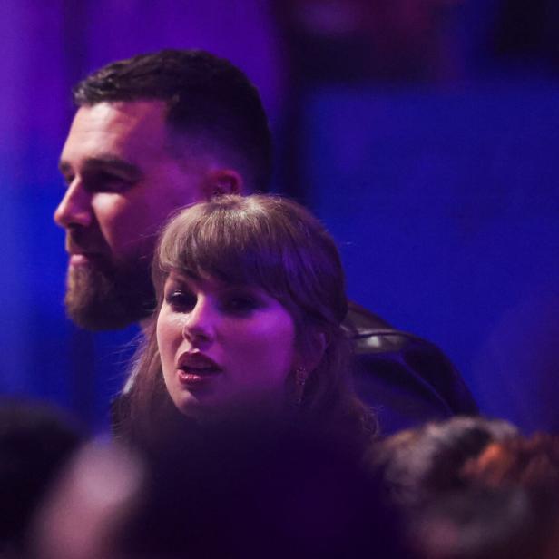 Taylor Swift und Travis Kelce stehen nebeneinander in einer Menschenmenge bei violettem Licht.
