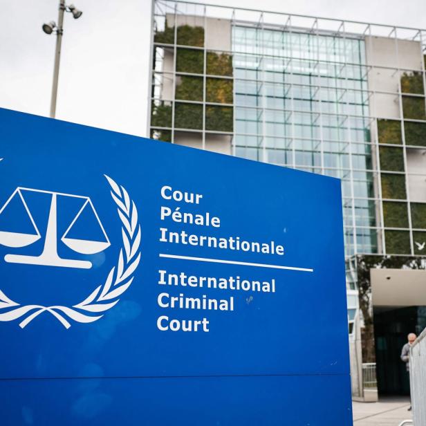 Blaues Schild mit dem Logo des Internationalen Strafgerichtshofs vor einem modernen Bürogebäude mit Glasfassade.