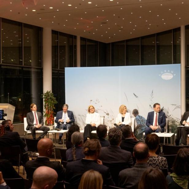 Podiumsdiskussion mit mehreren Teilnehmern vor Publikum im modern beleuchteten Saal.