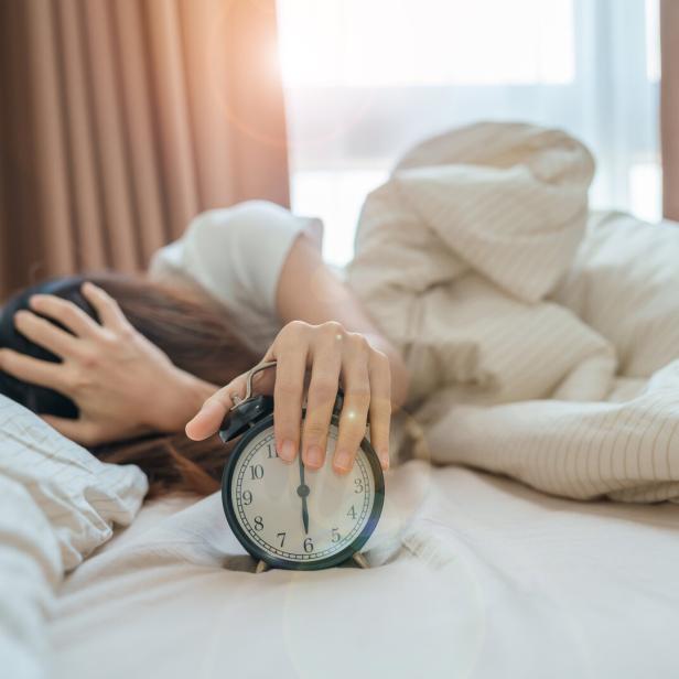 Eine Frau liegt im Bett und schlägt auf ihren Wecker. 