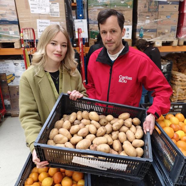 Zwei Personen halten eine Kiste mit Kartoffeln in einem Lagerraum mit Lebensmitteln.