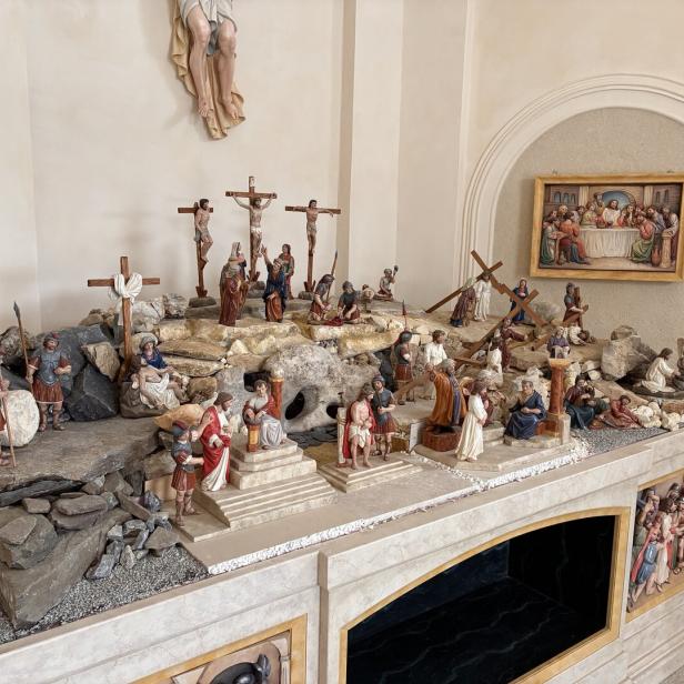 Mehrere Figuren stellen die Kreuzigung Jesu und Szenen seines Leidenswegs auf einem steinernen Podest mit Kreuzen und römischen Soldaten dar.