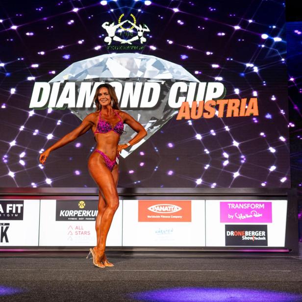 Eine Frau in einem lila Bikini posiert auf einer Bühne vor einem großen Schriftzug „Diamond Cup Austria“.