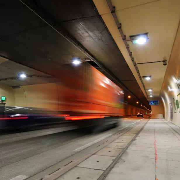 Ein Lastwagen fährt schnell durch einen beleuchteten Straßentunnel mit grünen Richtungsschildern an der Wand.