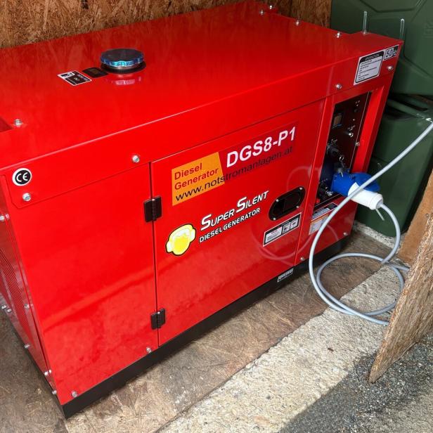 Roter Dieselgenerator mit der Aufschrift „Super Silent“ steht in einer Holzhütte und ist mit einem Stromkabel verbunden.