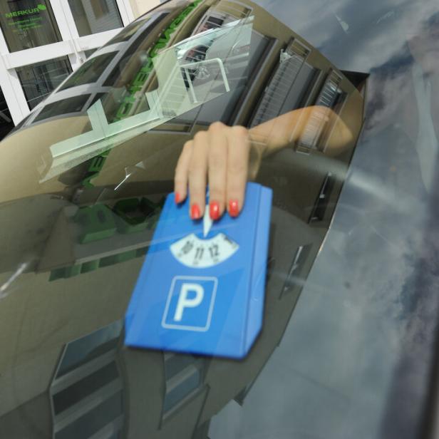 Eine Hand mit rotem Nagellack legt eine blaue Parkscheibe ins Auto.