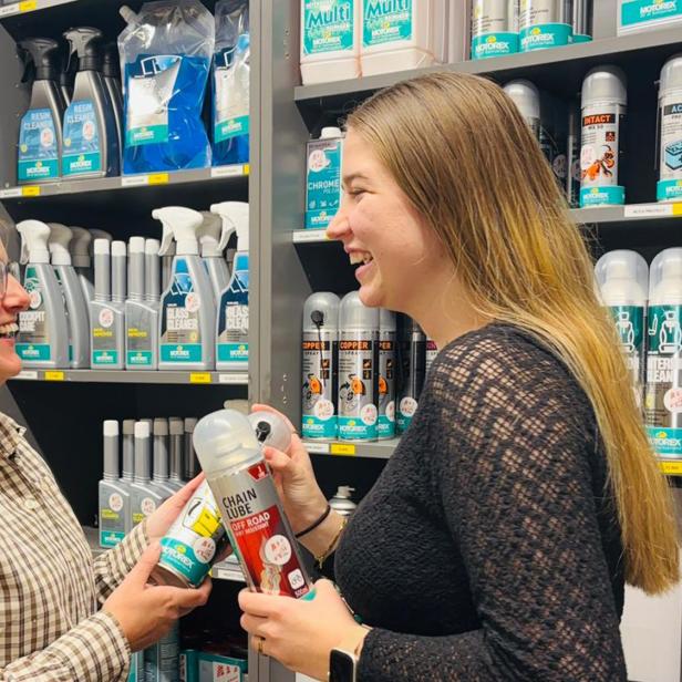 Zwei Frauen unterhalten sich lachend in einem Geschäft und halten Reinigungsprodukte in den Händen.