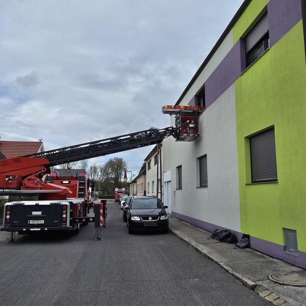 Ein Feuerwehrfahrzeug mit ausgefahrener Drehleiter steht vor einem Wohnhaus, die Leiter reicht zu einem Fenster im ersten Stock.