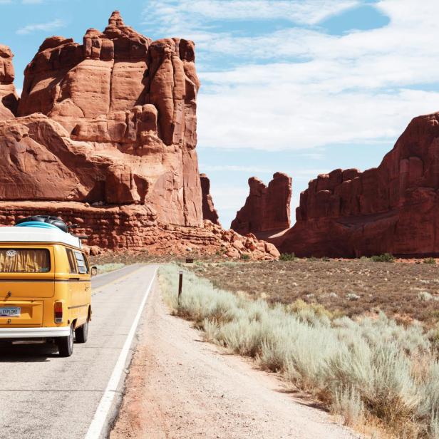Gelber Campingbus fährt auf Straße durch beeindruckende rote Felslandschaft bei sonnigem Wetter.