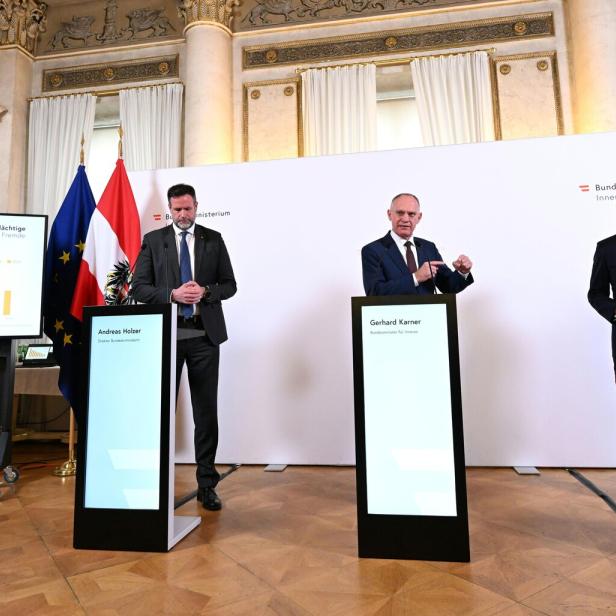 Drei Männer, darunter Gerhard Karner, stehen vor Flaggen und Bildschirmen bei einer Pressekonferenz.