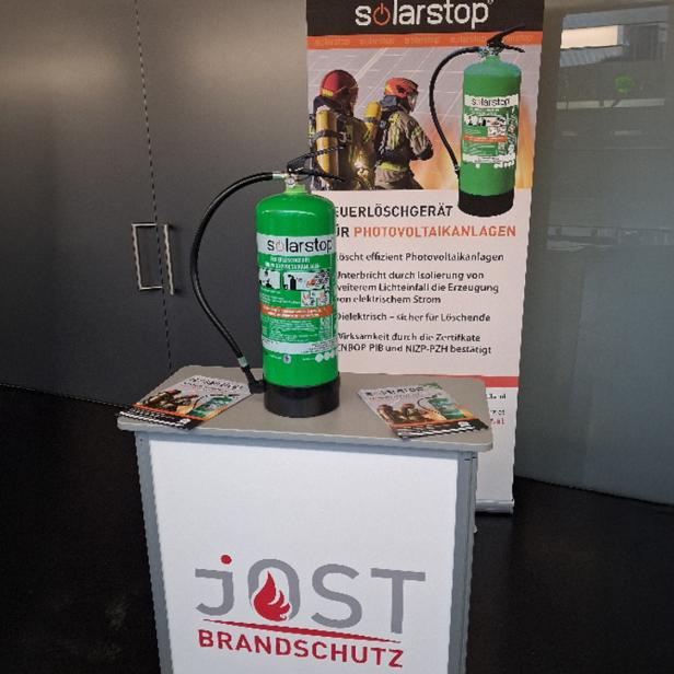 Ein grüner Feuerlöscher auf einem kleinen hohen Tisch vor einer Plakatwand