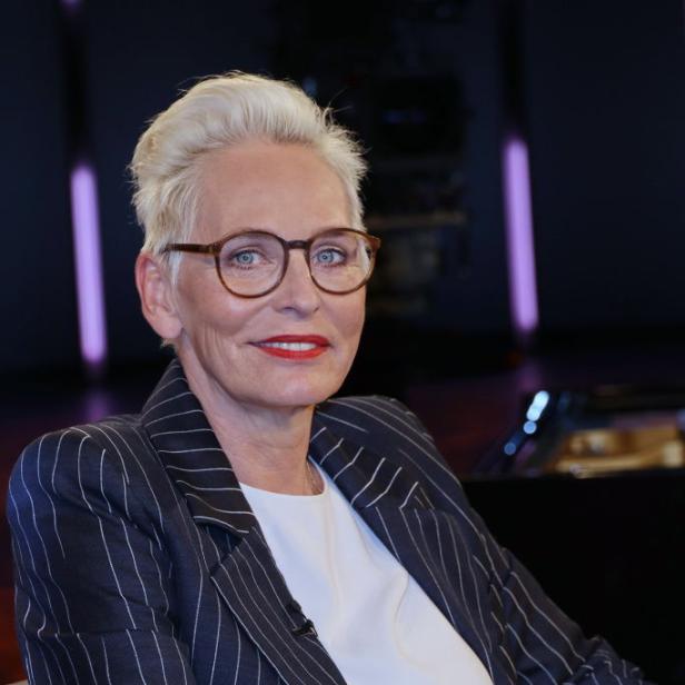 Bärbel Schäfer sitzt im gestreiften Blazer und mit rotem Lippenstift auf einem Sessel und blickt freundlich in die Kamera.