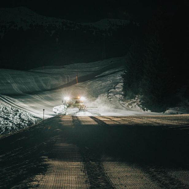 Beleuchtete Pistenraupe im Schnee bei Nacht