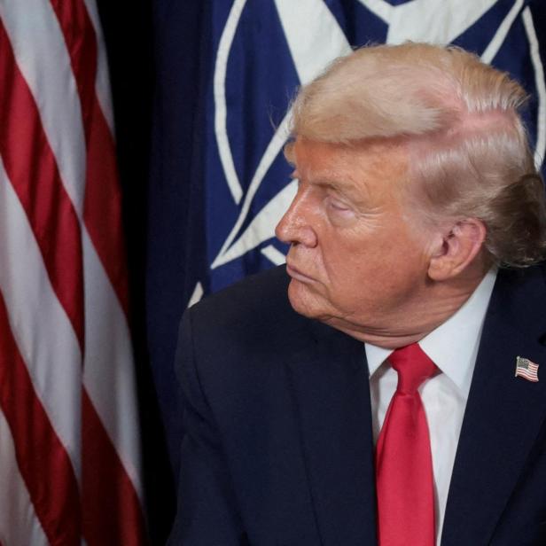 Donald Trump blickt vor Flaggen der USA und NATO nach links.