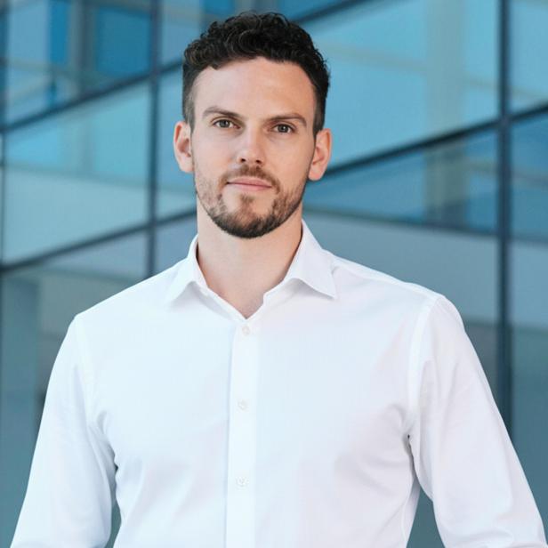 Mann im weißen Hemd steht vor moderner Glasfassade eines Bürogebäudes.