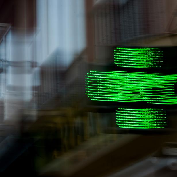 Verschwommenes grünes LED-Kreuz leuchtet vor unscharfem Hintergrund in einer Stadt.