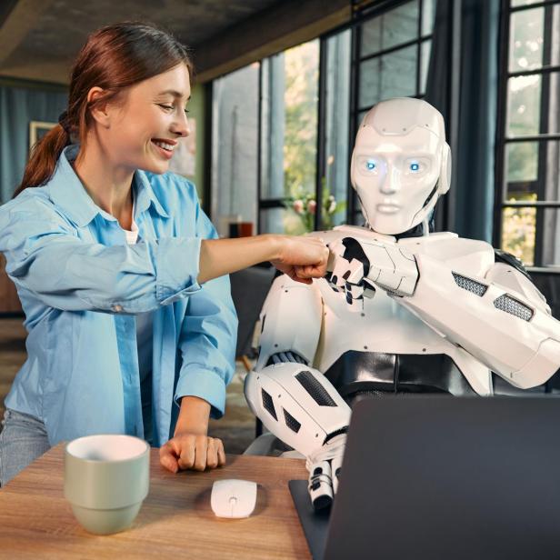 Frau und humanoider Roboter geben sich im Büro einen freundschaftlichen Faustgruß.