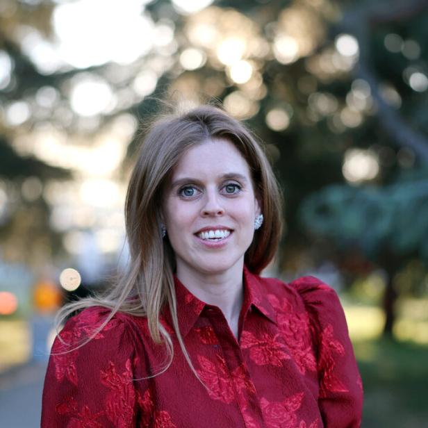 Prinzessin Beatrice mit blonden Haaren trägt ein rotes, geblümtes Kleid mit Gürtel.