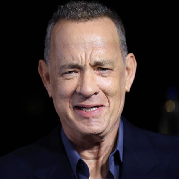 Tom Hanks lächelt vor einem dunklen Hintergrund.