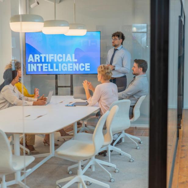 Fünf Personen diskutieren in einem modernen Konferenzraum vor einem Bildschirm mit „Artificial Intelligence“.