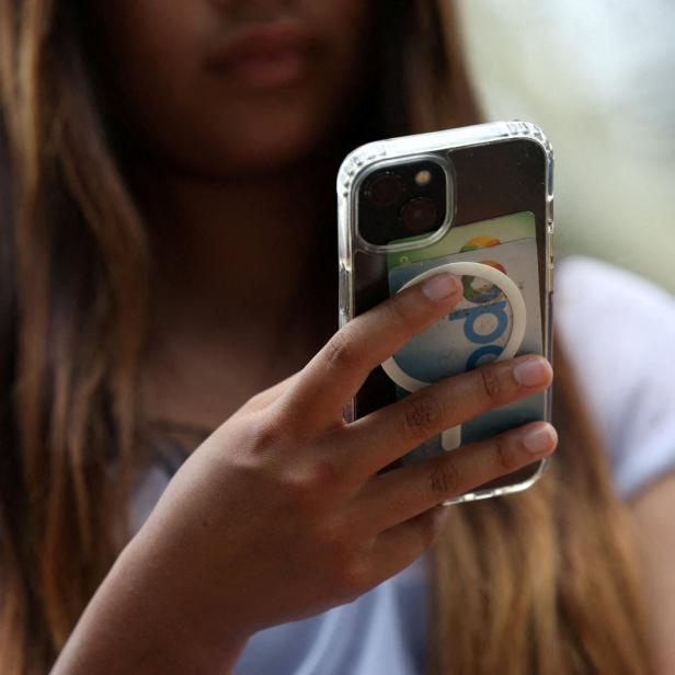 Eine Person mit langen Haaren hält ein Smartphone mit transparentem Case in der Hand.