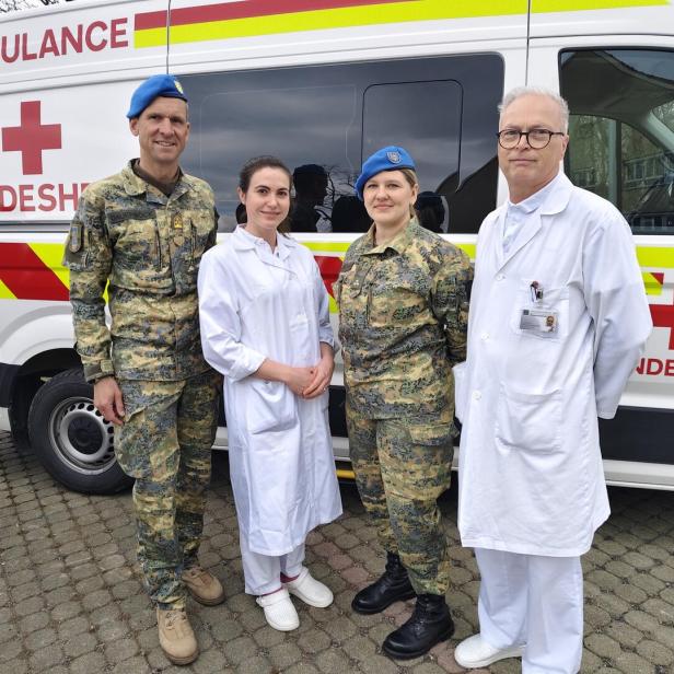 Zwei Personen in Militäruniform und zwei in weißer Kleidung stehen vor einem Rettungswagen mit der Aufschrift „Bundesheer“.