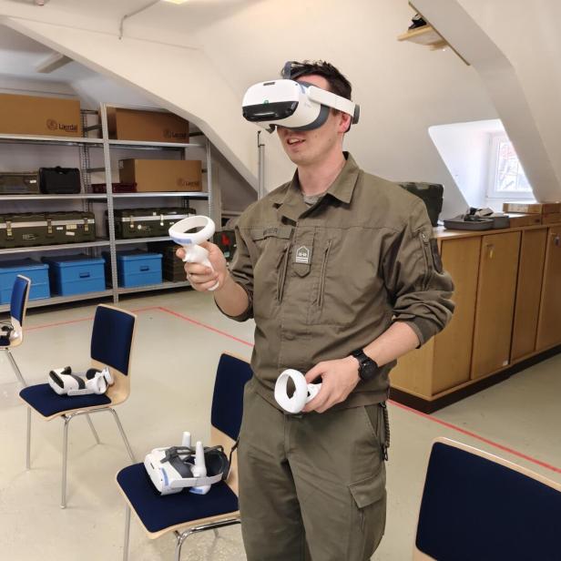 Eine Person in Uniform nutzt eine Virtual-Reality-Brille mit Controllern in einem Raum mit Stühlen und Regalen.