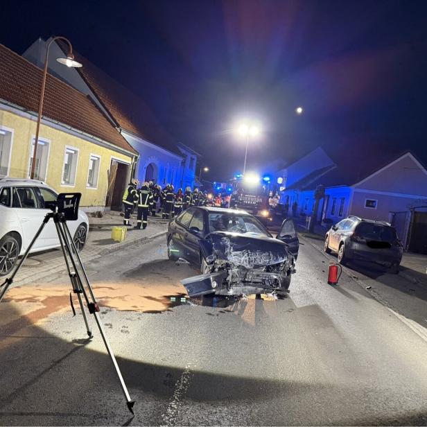 Ein Unfallauto mit stark beschädigter Front steht auf einer nächtlichen Straße, umgeben von Feuerwehrleuten und Einsatzfahrzeugen.