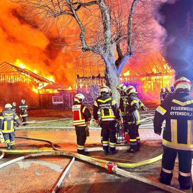 Mehrere Feuerwehrleute bekämpfen einen Großbrand in einem brennenden Gebäude bei Nacht.