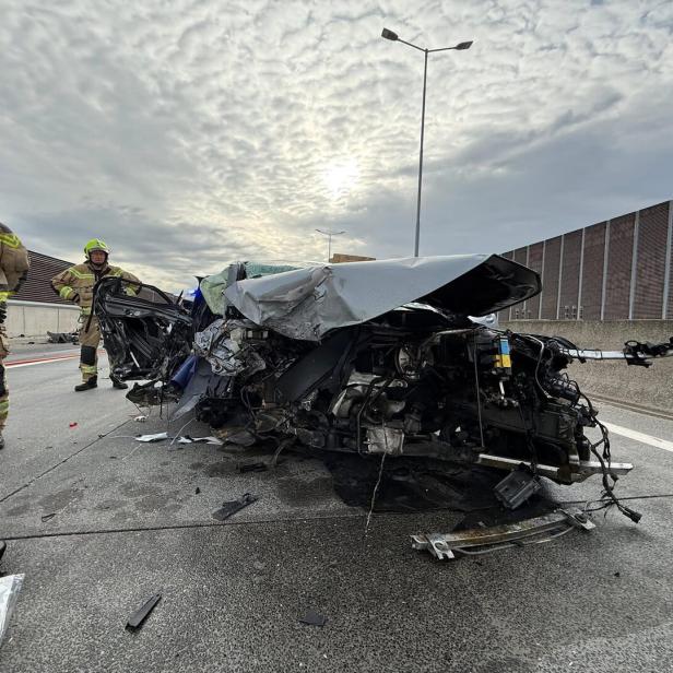 Zwei Feuerwehrleute stehen neben einem stark zerstörten Autowrack auf einer Autobahn.