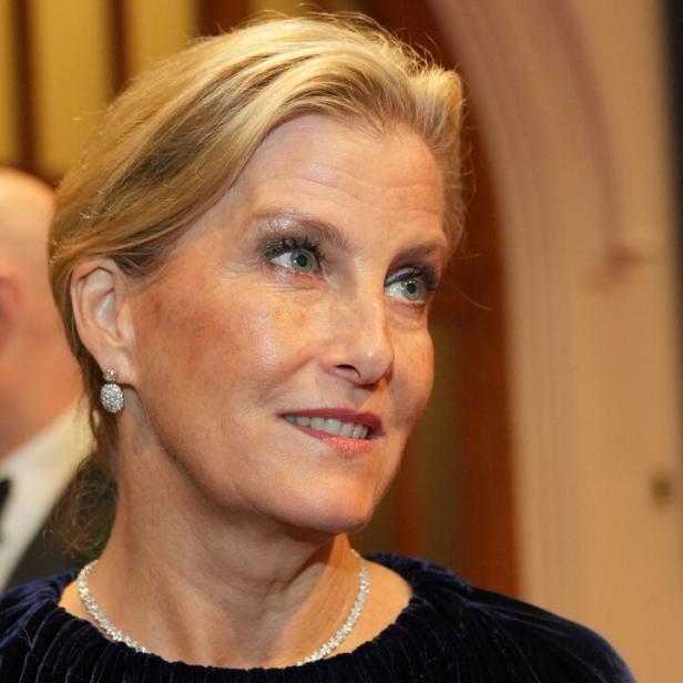 Herzogin Sophie mit Halskette und Brosche in Marineblau blickt lächelnd zur Seite.