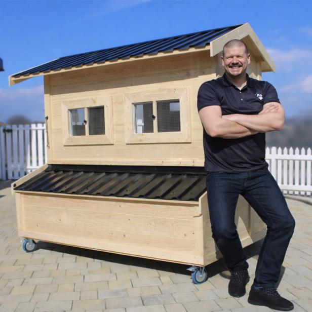 Mann steht lächelnd vor einem großen, mobilen Hühnerstall aus Holz im Freien.