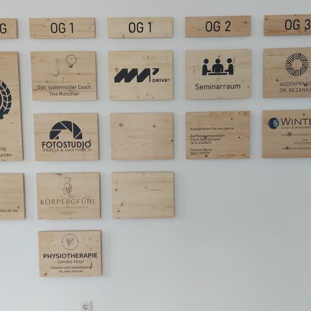 Holzschilder mit verschiedenen Firmenlogos und Beschriftungen an einer weißen Wand montiert.