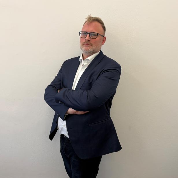 Ein Mann lehnt in einem Anzug an einer Wand 