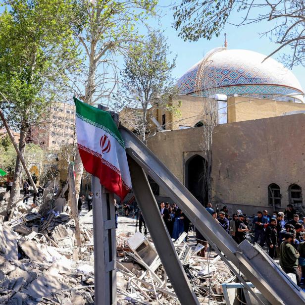 Zerstörtes Gebäude, im Vordergrund eine Flagge, im Hintergrund eine Moschee