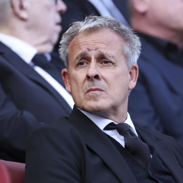 Pierre Littbarski mit grauem Haar und dunklem Anzug schaut aufmerksam zur Seite.