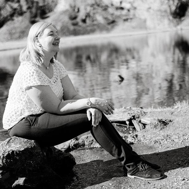 Eins chwarz-weißes-Bild einer Frau, die an einem Wasser auf einem Baumstamm sitzt