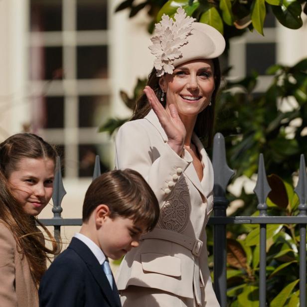 Kate, Charlotte und George winken freundlich hinter einem Zaun.