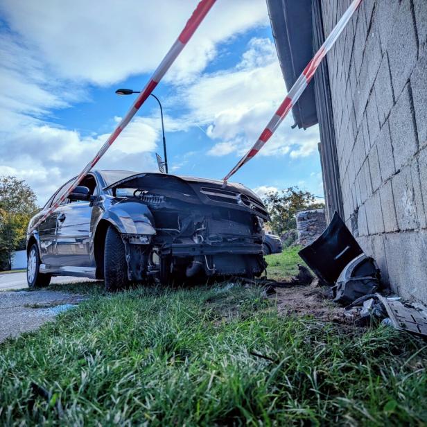 Ein Auto mit beschädigter Front steht neben einer Mauer, Trümmerteile liegen auf dem Boden, Absperrband ist gespannt.